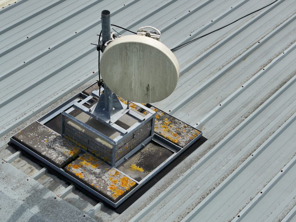 A close-up inspection image showing a roof-mounted antenna and its weighted base on the steel-clad hangar roof
