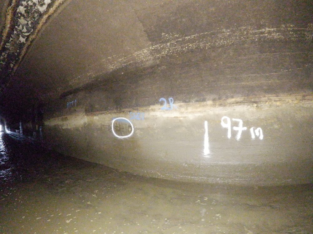 Interior view of the historic Ardnacrusha head race canal showing water flow and painted inspection markings on weathered concrete walls