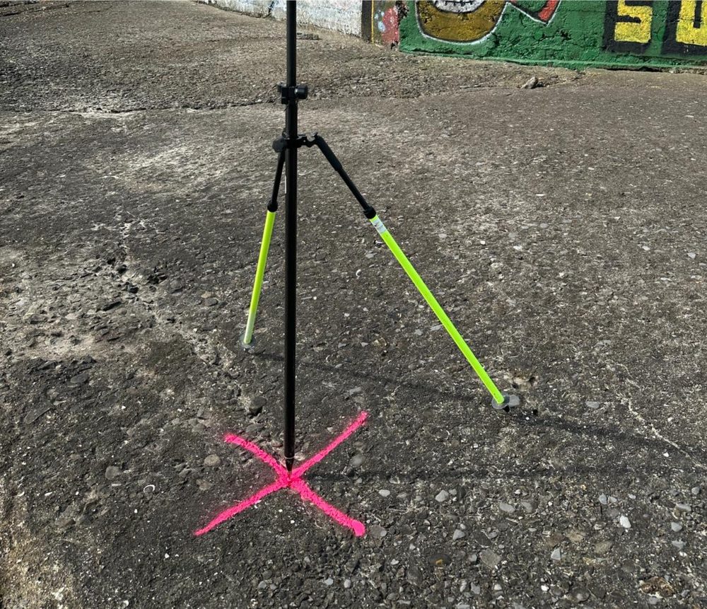 A ground control point mounted on a tripod over a spray-painted survey cross marking its position on the coastal ground