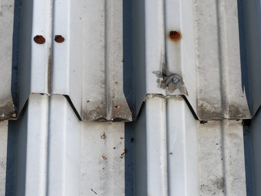 Close-up drone image of heavily corroded fixing heads on roof sheeting, with rust staining running down the surface