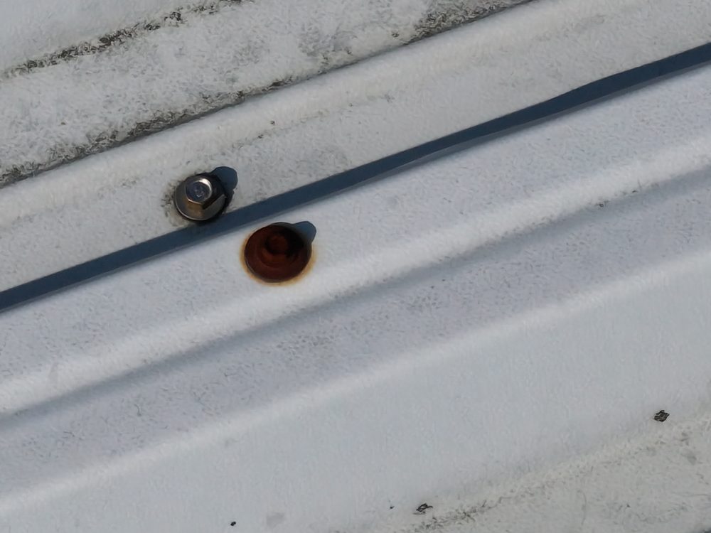 Close-up drone image of two fixings on a roof seam, one with a corroded ring around the fastener