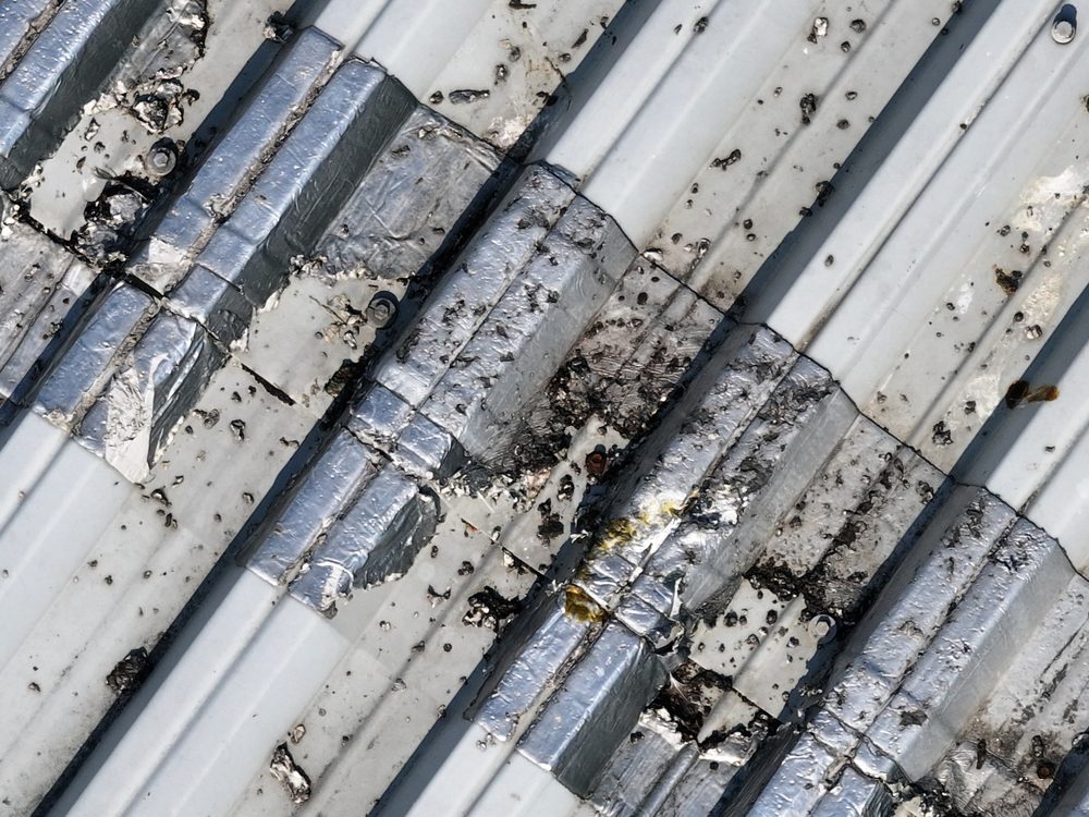 Close-up drone image of a roof sheet joint covered with aluminium foil tape, with corrosion and a build-up of debris along the joint