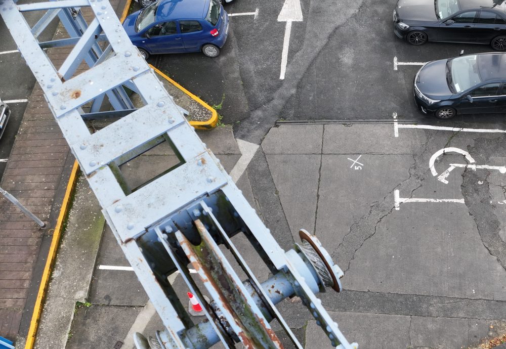 Aerial view of the old ship-loading crane from above, with the river to the left and a car park below and to the right