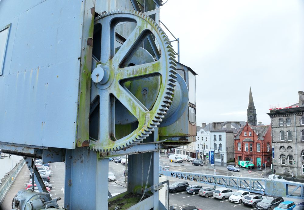 A weathered pulley wheel on the crane framework with the town waterfront behind