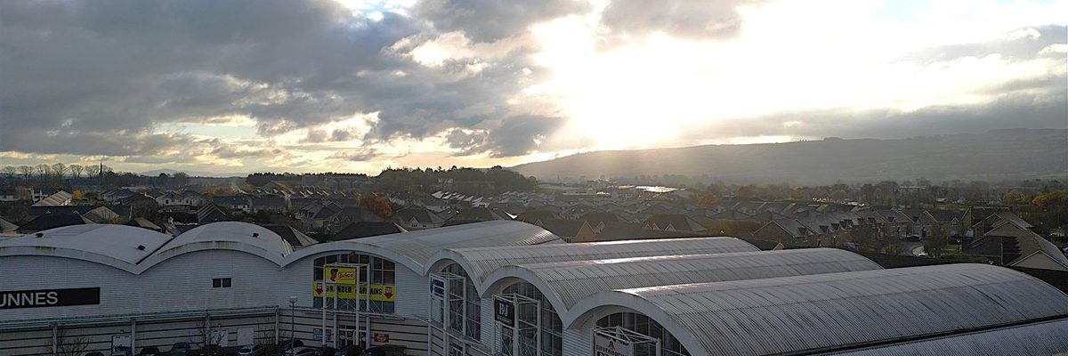 Aerial view of a commercial shopping estate in Co. Carlow, showing the distinctive curved roof structures across multiple buildings