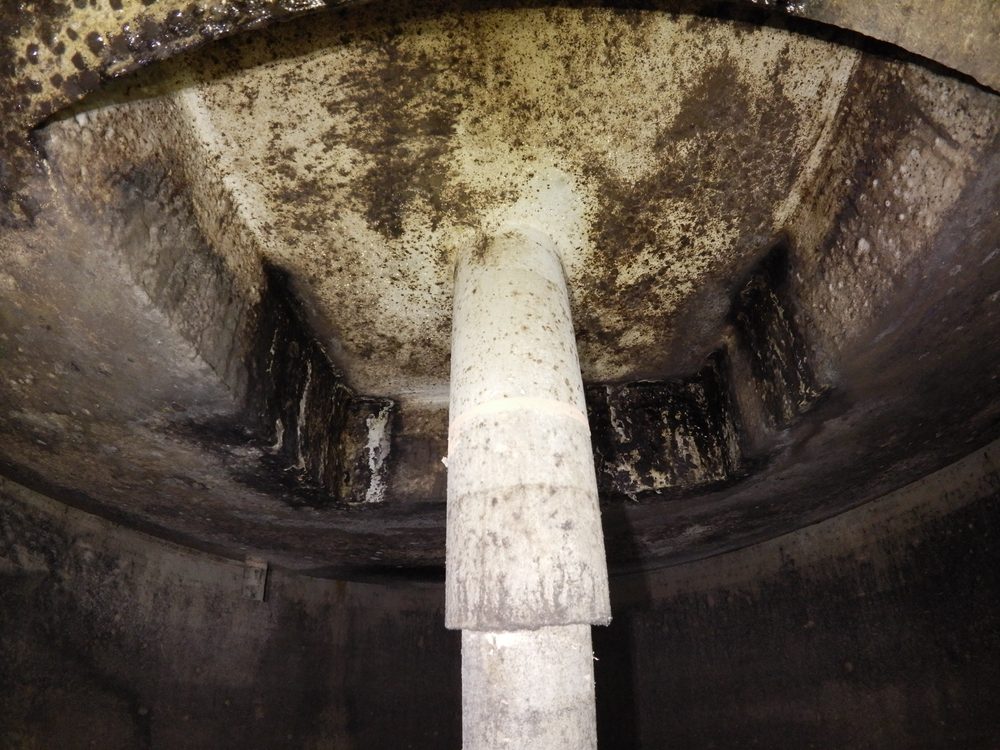 Close-up drone image of a commercial roof showing significant debris accumulation and discolouration along the gutter and flashing at a building junction