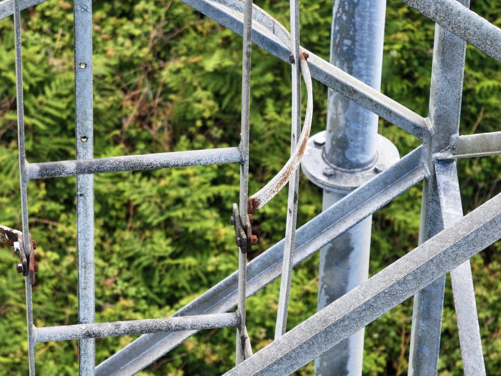 A close-up looking up through the grey steel lattice of the tower, showing the cross-bracing and a vertical cable