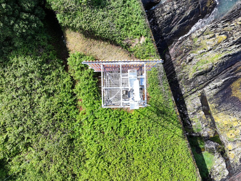 A high-angle aerial view looking straight down on the platform and top of the lattice tower, surrounded by dense vegetation