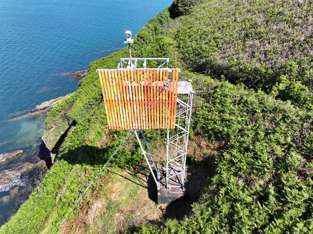 An aerial view of the large orange slatted board mounted on its steel framework on a grassy slope beside the water