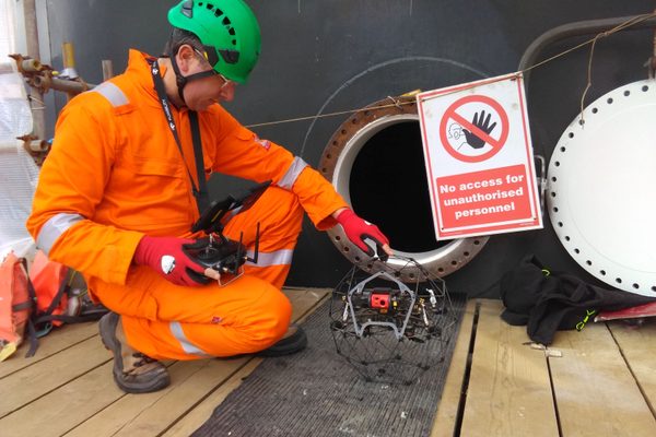 A man with a confined space drone in front of some oil and gas infrastructure